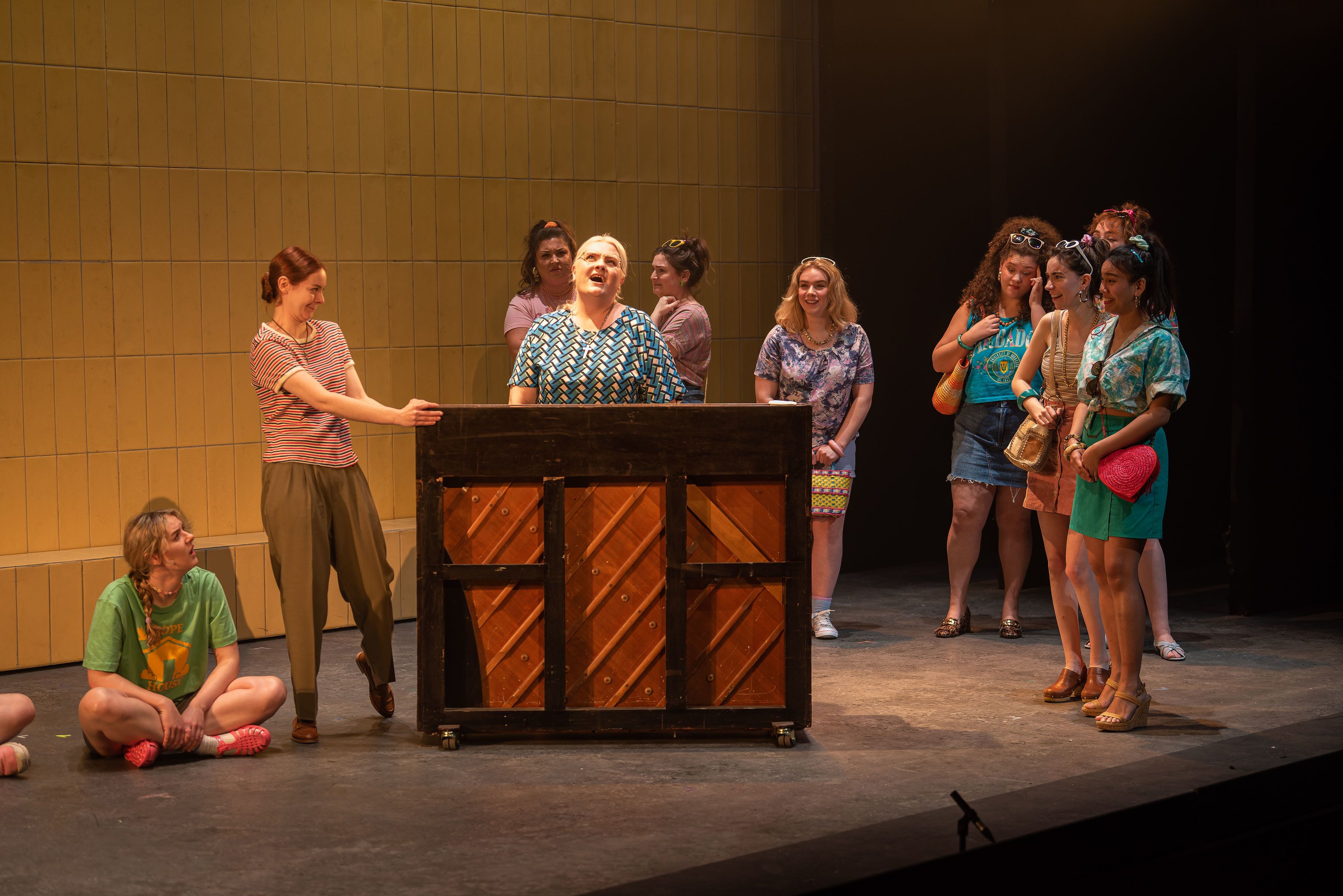 Women standing and singing around a piano