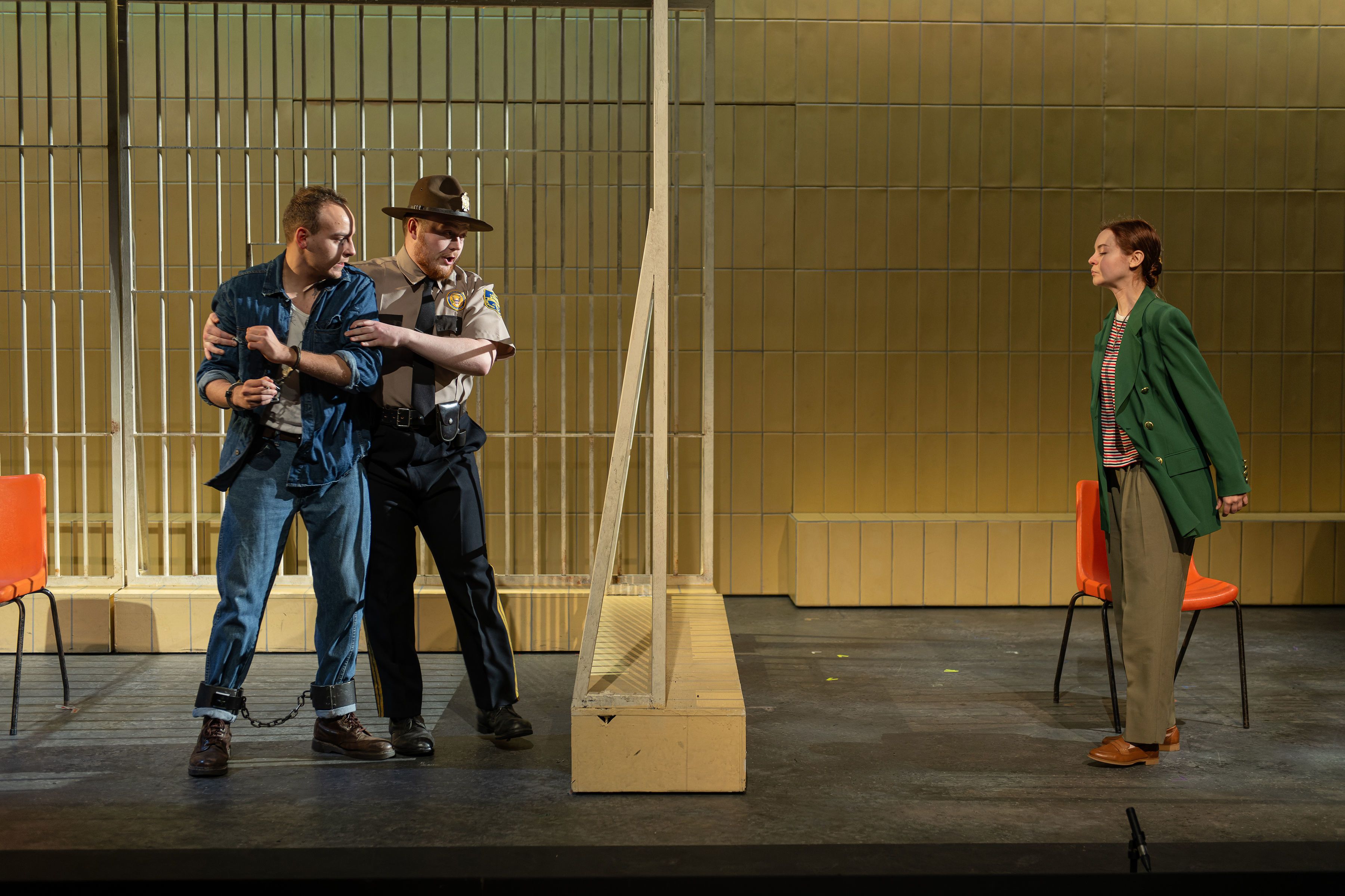 A guard restrains a prisoner in prison, and woman standing on the other side of the bars
